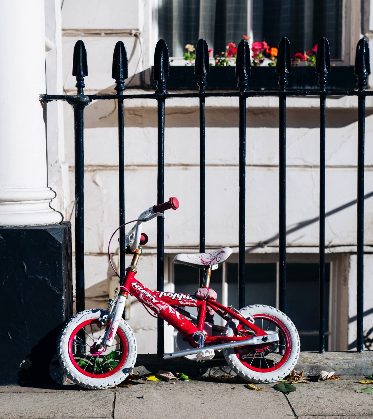 Picture of a toddler's red bike leaning against a fence.